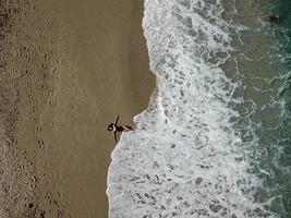 vista aérea superior jovem deitada na praia de areia e ondas foto
