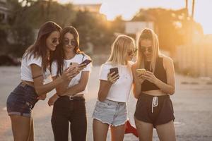 quatro mulheres atraentes estão de pé no estacionamento com smartphones foto