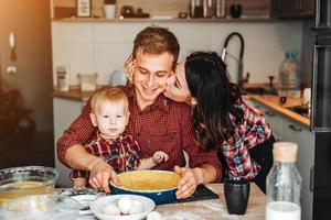 pai, mãe e filho pequeno cozinham uma torta foto