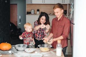 pai, mãe e filho pequeno cozinham uma torta foto