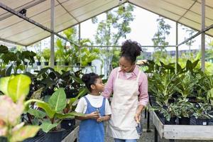 mãe africana está ensinando sua filha a cultivar plantas ornamentais em seu próprio centro de jardim de berçário cheio de plantas exóticas e tropicais foto