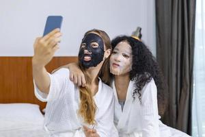 casal de namoradas em roupão de banho tomando selfie fazendo rotina de cuidados com a pele usando máscara facial em férias de spa para pele de beleza e conceito de tratamento foto