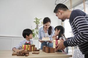 feliz família tailandesa asiática, filha jovem é surpreendida com bolo de aniversário e presente, sopra vela, reza e alegre celebra festa com os pais juntos na mesa de jantar, estilo de vida de eventos domésticos domésticos. foto