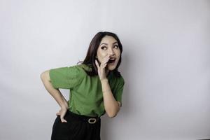 jovem mulher bonita vestindo uma camiseta verde gritando e gritando alto com a mão na boca dela. conceito de comunicação. foto