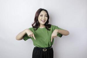 mulher asiática animada vestindo camiseta verde apontando para o espaço de cópia ao lado dela, isolado por fundo branco foto