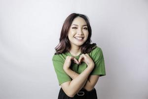 uma jovem asiática atraente vestindo uma camiseta verde se sente feliz e um gesto de coração de formas românticas expressa sentimentos ternos foto