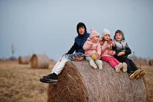 quatro crianças com frutas nas mãos, sentado no feno no campo. foto