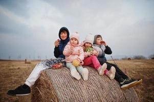 quatro crianças com frutas nas mãos, sentado no feno no campo. foto