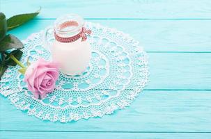 hora do almoço com jarro de leite, rosa rosa e fita xadrez sobre fundo azul de madeira. toalha de renda. foco seletivo. dia dos namorados e das mães foto