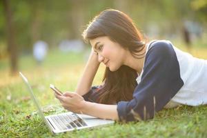 garota atraente joga celular com laptop no jardim foto