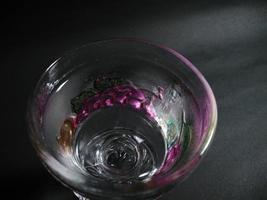 um copo transparente estampado de frutas cheio de água mineral em um fundo preto. foto