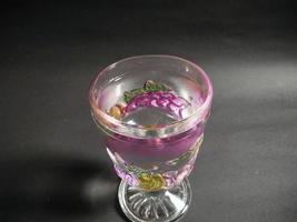 um copo transparente estampado de frutas cheio de água mineral em um fundo preto. foto