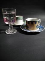 xícara de chá, xícara de café e vidro estampado de frutas transparente cheio de água mineral em um fundo preto. foto
