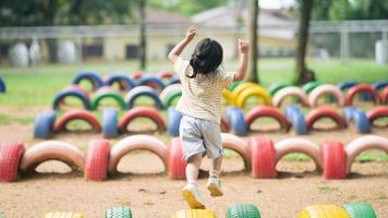 linda garota asiática sorri e brinca na escola ou jardim de infância ou playground. atividade de verão saudável para crianças. menina asiática escalando ao ar livre no playground. foto