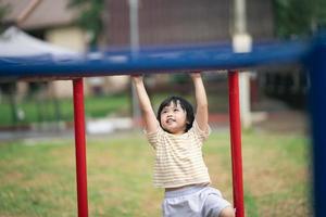 linda garota asiática sorri e brinca na escola ou jardim de infância ou playground. atividade de verão saudável para crianças. menina asiática escalando ao ar livre no playground. foto