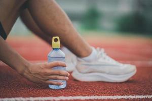 atletas corredor esporte homem descansando segurando garrafa de água cansado e com sede praticando em uma pista de corrida em um estádio. água potável de treino de corrida. conceito de corrida de homem esportivo. foto