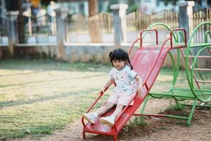 sorriso de linda garota asiática brinca na escola ou jardim de infância ou playground. atividade de verão saudável para crianças. menina asiática escalando ao ar livre no playground. criança brincando no playground ao ar livre. foto