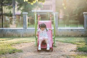 sorriso de linda garota asiática brinca na escola ou jardim de infância ou playground. atividade de verão saudável para crianças. menina asiática escalando ao ar livre no playground. criança brincando no playground ao ar livre. foto