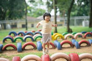 linda garota asiática sorri e brinca na escola ou jardim de infância ou playground. atividade de verão saudável para crianças. menina asiática escalando ao ar livre no playground. foto