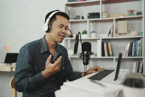 homem asiático usando fones de ouvido brancos toca piano e canta uma música aprendendo on-line com o celular ou grava som com um microfone e usa o programa de música de gravação de computador. engenheiro de som gravar música foto