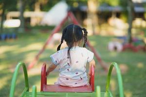 vista traseira sorriso menina asiática jogar na escola ou jardim de infância ou parque infantil. atividade de verão saudável para crianças. menina escalando ao ar livre no playground. criança brincando no playground ao ar livre. foto