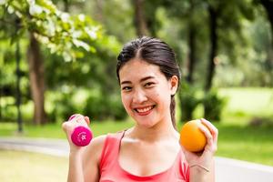 retrato de mulher atraente está segurando haltere e laranja no parque. foto