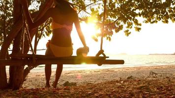 mulher sexy em trajes de banho amarelos sentado no balanço na praia. foto