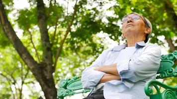 homem asiático feliz sentado em um banco no parque. foto