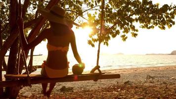 mulher sexy em trajes de banho amarelos sentado no balanço na praia. foto