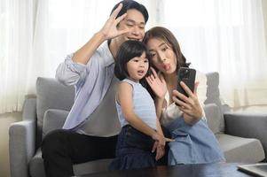 família asiática com crianças segurando smartphone e fazendo videochamada em casa foto