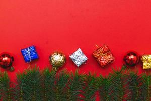 vista superior de bolas vermelhas de caixa de presente de natal com ramos de abeto, pinhas, bagas vermelhas e sino em fundo vermelho. foto