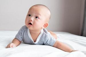 bebê retrato em uma camisa listrada, vista frontal, rastejando em um colchão branco foto