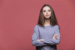 retrato de empresária séria sendo segura de si mesma, mantém os braços cruzados, usa suéter casual, tem cabelos escuros, modelos contra fundo rosa com espaço de cópia para seu conteúdo publicitário foto