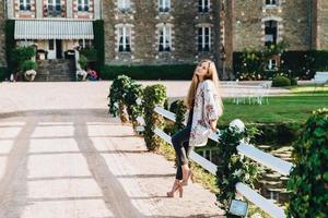 mulher descansada passa seu tempo livre, caminha perto do antigo castelo de tijolos, inclina-se para o branco, usa roupas da moda e sapatos de salto alto, gosta de dia ensolarado e belo exterior ao ar livre foto