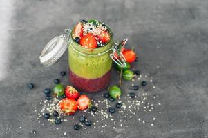 pote de smoothie de frutas com frutas exóticas morango, groselha e mirtilo com flocos de coco isolados sobre fundo cinza. sobremesa deliciosa foto