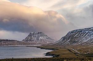sob uma espetacular paisagem de nuvens típica dos dias de inverno islandês, a estrada que leva a kirkjufell segue a forma do fiorde. foto
