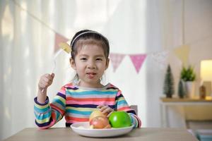 menina asiática de criança comendo maçã na mesa, conceito de hábitos alimentares saudáveis foto