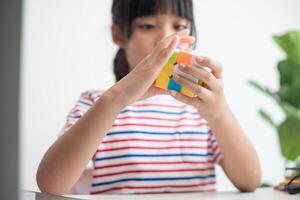 menina bonitinha asiática segurando o cubo de rubik nas mãos dela. cubo de rubik é um jogo que aumenta a inteligência das crianças. foto