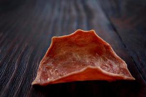 chips de carne. um único pedaço de carne seca encontra-se em um fundo escuro de madeira. foto