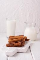 churros caseiros com leite e creme em um fundo branco de madeira. foto