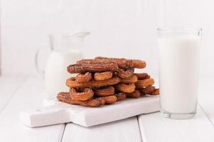 churros caseiros com leite e creme em um fundo branco de madeira. foto