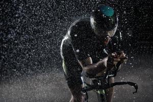 atleta de triatlo andando de bicicleta rápido na noite chuvosa foto