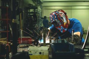 soldador profissional da indústria pesada trabalhando dentro da fábrica, usa capacete e começa a soldar. foco seletivo foto