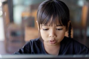 menina criança asiática feliz olha para tablet em cima da mesa foto