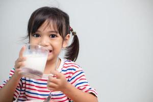 menina bonita criança asiática comendo legumes saudáveis e leite para sua refeição foto