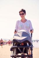 mãe andando na praia e empurra o carrinho de bebê foto