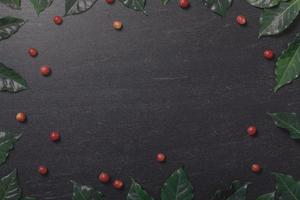 fechar grãos de café vermelhos orgânicos frescos com folhas de café em fundo preto com espaço de cópia foto