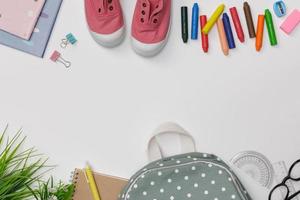 flatlay criativo de mesa branca de educação com mochila, livros de estudante, sapatos, giz de cera colorido, óculos, espaço vazio isolado no fundo branco, conceito de educação e volta às aulas foto