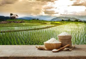 arroz de jasmim na tigela e saco na mesa de madeira com o fundo do campo de arroz foto