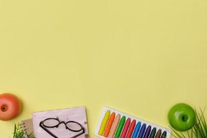 flatlay criativo de mesa amarela de educação com livros de estudante, giz de cera colorido, óculos, espaço vazio isolado em fundo amarelo, conceito de educação e volta às aulas foto